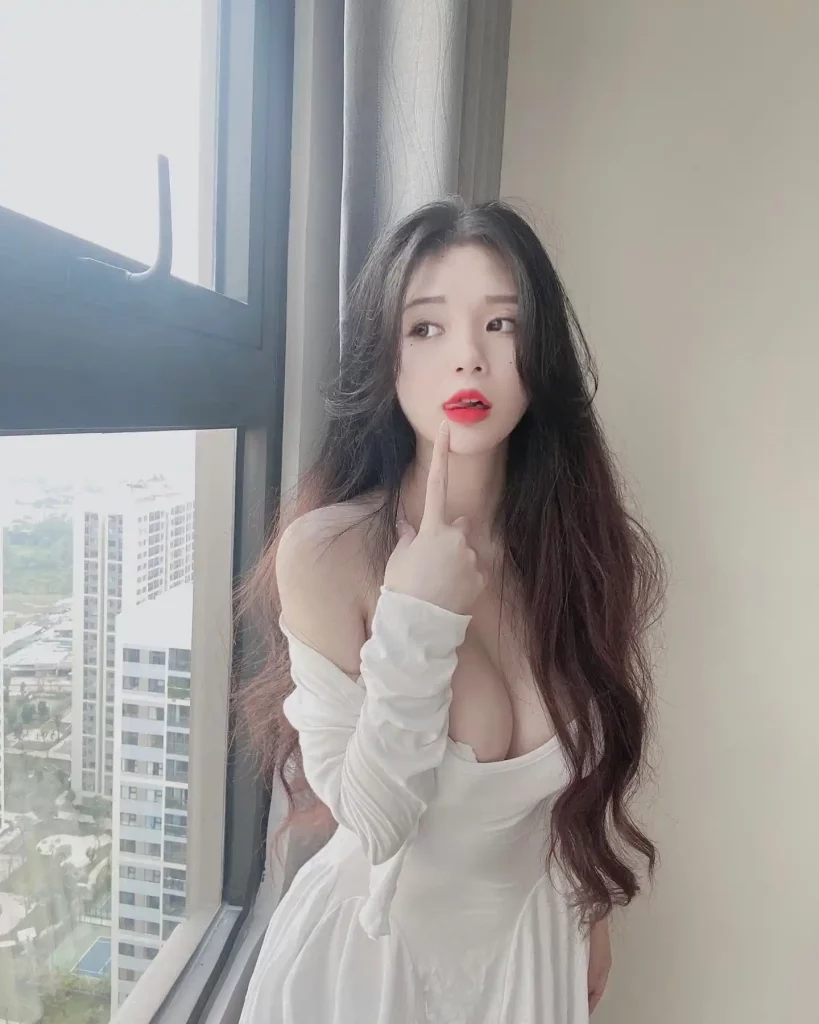 Nhung Dory đứng bên cửa sổ với chiếc đầm trắng trễ vai